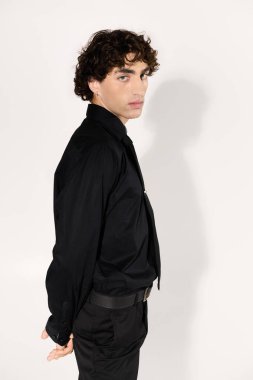 Modaya uygun genç bir adam, kendine güvenen siyah bir elbiseyle duruyor, tarzını ve çekiciliğini vurguluyor..