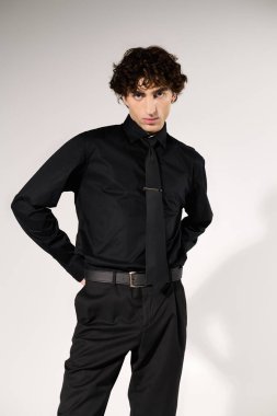 Siyah giyinmiş yakışıklı genç adam, basit bir arkaplanda rahatça poz veriyor..