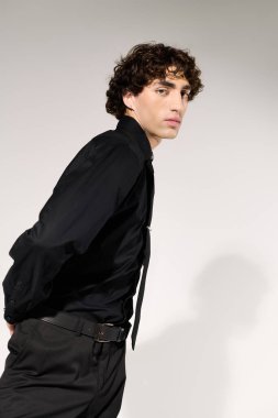 Zarif giyinmiş genç yakışıklı bir adam minimalist bir arka plana karşı güvenle duruyor..