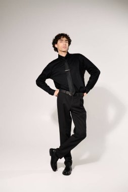 Genç ve yakışıklı bir adam şık siyah bir elbiseyle moda anlayışını sergiliyor. Kendine güveni tam..