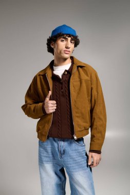 Kendine güvenen, modaya uygun giyinmiş genç bir adam tarafsız bir arkaplan karşısında poz veriyor..