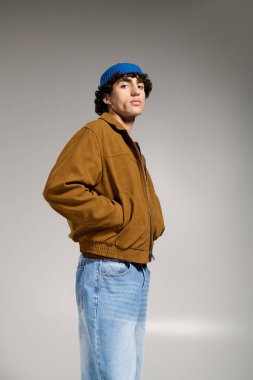 Genç adam stil ve çekicilik sergiliyor, minimalist bir stüdyoda kendine güvenen modaya uygun bir şekilde poz veriyor..