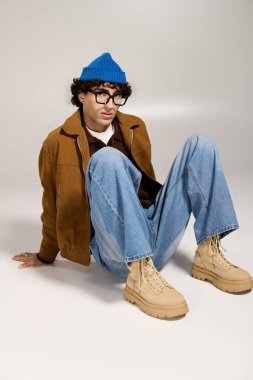 Şık bir genç adam modaya uygun giysiler içinde gevşiyor ve neşeli mavi bir bere takıyor..