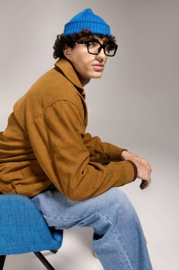 Genç yakışıklı bir adam bir sandalyede oturuyor, şık kıyafetler ve şık bir hava sergiliyor..