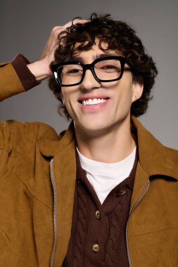 Genç bir adam moda anlayışını, kıvırcık saçlarıyla ve şık gözlükleriyle eğlenceli bir anda sergiliyor..