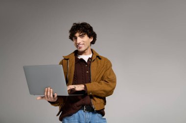 Moda kıyafetli genç adam dizüstü bilgisayarıyla meşgul, kendine güven ve tarz yayıyor..