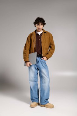 Kendine güveni tam genç bir adam şık kıyafetler içinde elinde bir dizüstü bilgisayarla şık bir ortamda duruyor..