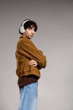 Kendine güvenen genç adam, sanatsal bir stüdyo ortamında moda kıyafetler ve kulaklıklar sergiliyor..