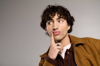 Moda elbiseli genç adam neşeli bir poz veriyor, stüdyoda eğlenceli bir hava yaratıyor..