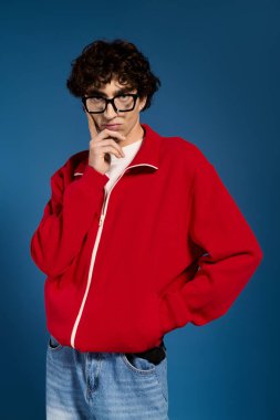 Şık kırmızı elbiseli genç bir adam, gösterişli tarzı ve kendine güveni olan oyuncu bir poz veriyor..