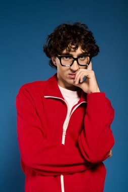 Kıvırcık saçlı ve gözlüklü düşünceli genç bir adam şık kırmızı kıyafetiyle hava atıyor..