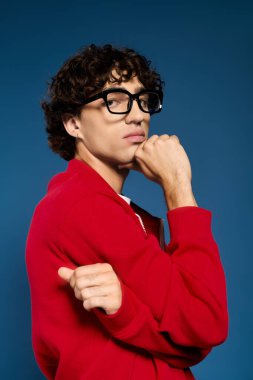 Kırmızı ceketli ve gözlüklü yakışıklı genç bir adam mavi karşısında kendine güvenen bir duruş sergiliyor..