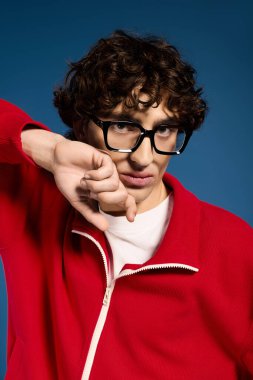 Şık bir genç adam parlak kırmızı bir elbise ve neşeli gözlüklerle rahatça poz verir..