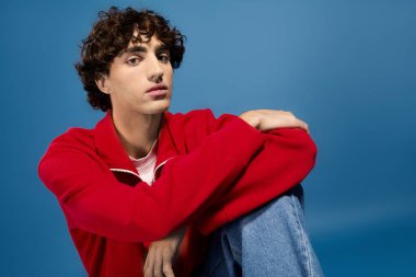 Şık bir genç adam kırmızı bir kazak ve kot pantolon içinde kendinden emin bir şekilde poz verir..