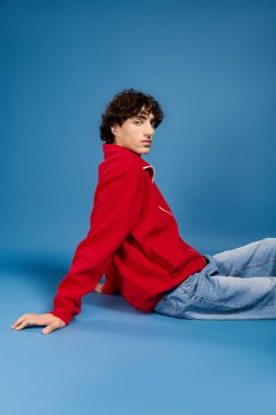 Kendine güveni olan genç adam, modaya uygun kırmızı elbiseler içinde mavi arka planda, tarzını sergiliyor..