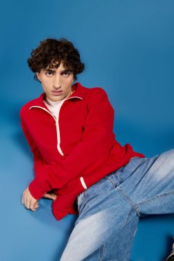 Moda kıyafetli yakışıklı adam cesur mavi bir arka plana çarpıcı bir poz sergiliyor.