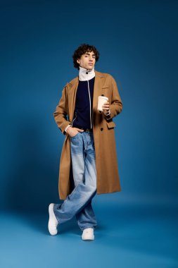 Şık bir genç adam mavi bir fonda kendine güvenerek bir kahve fincanı tutuyor..