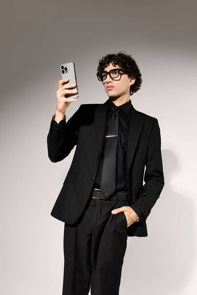Молодой человек во всем черном уверенно проверяет свой смартфон, подчеркивая свое чувство стиля.