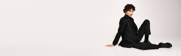 Handsome young man in sleek attire poses effortlessly in a minimalistic environment, exuding style.