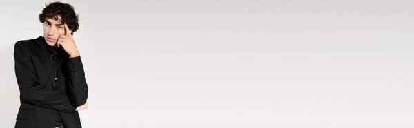 Confident young man in fashionable black suit expresses deep thought with a stylish pose.