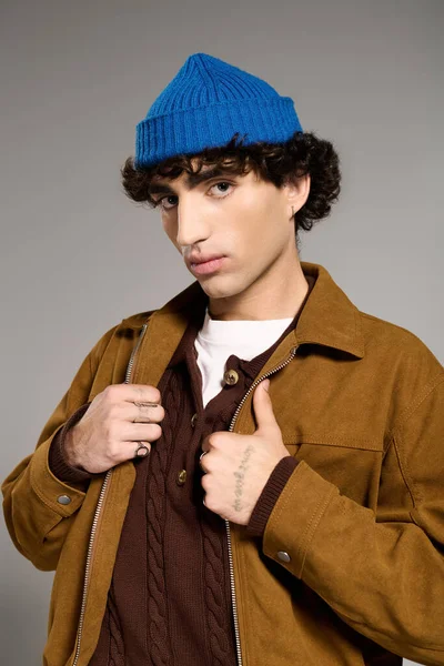 Rahat kahverengi ceketli ve mavi bereli yakışıklı bir adam çağdaş bir stüdyoda rahatça poz veriyor..