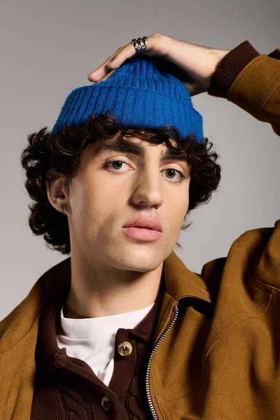 Yakışıklı genç adam kendine güvenerek poz veriyor, mavi bir bere takıyor ve şık giyiniyor, çekicilik getiriyor..