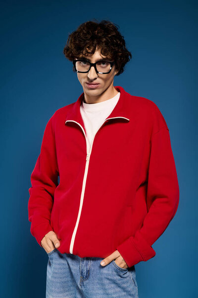 Handsome man poses confidently in stylish red sweater and denim, exuding modern fashion flair.