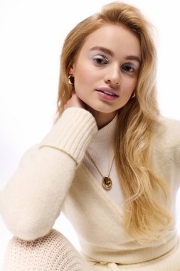 Genç sarışın kadın beyaz bir arka plana karşı şık bir kış elbisesi mankenliği yapıyor..