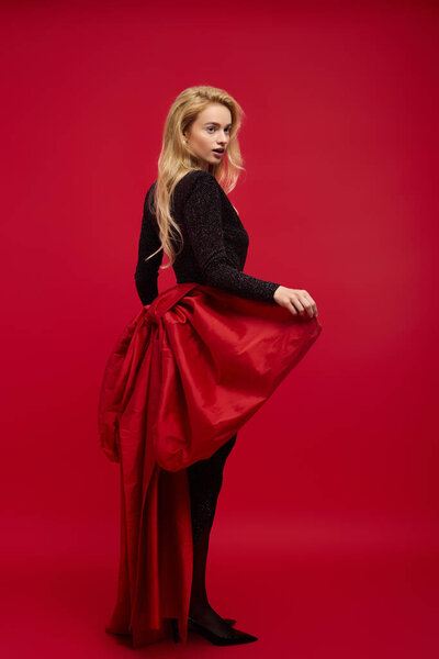 Стильная блондинка изящно позирует на ярком красном фоне на зимнем празднике.