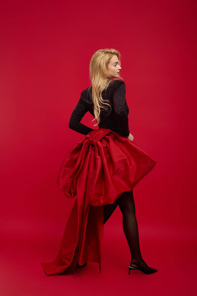 Молодая женщина элегантно позирует в потрясающем черном наряде с красной юбкой, олицетворяя праздничный дух.
