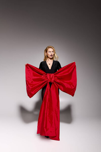 Блондинка изящно позирует в черном наряде с праздничным красным бантом на праздники.