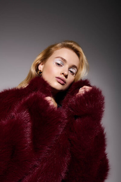 Стильная блондинка позирует в ярком красном шубе зимой.