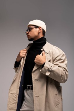 Moda kıyafetleri içindeki genç adam şık bir şekilde minimalist bir stüdyoda poz veriyor..