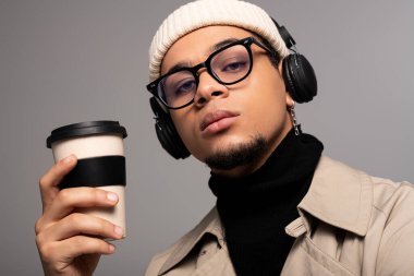 Yakışıklı genç adam kahve içer, şık kıyafetler giyer ve şık kulaklıklar takar..