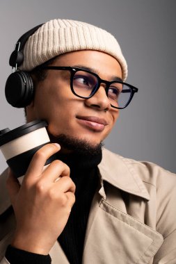 Genç adam nefis bir içecek yudumluyor, modaya uygun kıyafetler ve kulaklıklar takıyor..