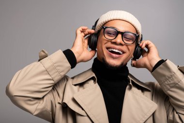 Şık giyinmiş genç adam kulaklıkla müzik dinlerken gülümsüyor..