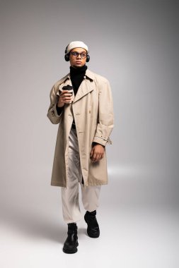 Genç adam şık bir kıyafetle, kahvesini yudumlayarak ve kulaklık takarak güvenle yürüyor..