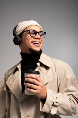 Yakışıklı genç adam elinde kahve fincanı tutarken gülümsüyor, modern moda ve kulaklık takıyor..