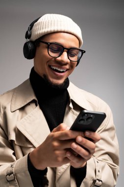 Şık genç adam gülümsüyor, telefonuna bakarken kulaklıkla müzik dinliyor..