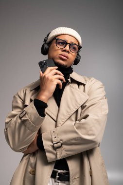 Moda ceketli şık bir genç adam elinde akıllı bir telefonla düşünceli bir şekilde poz verir..