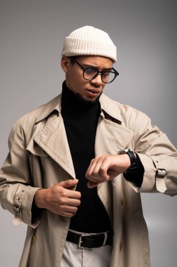 Yakışıklı bir genç saatini inceliyor, stüdyo ortamında çağdaş tarzını sergiliyor..