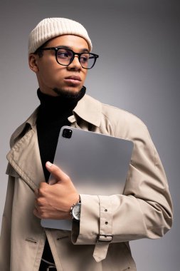 Tarz sahibi genç bir adam, elinde bir tablet tutarak, kendine güvenerek poz verir ve modern kıyafetler giyer..