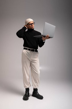 Şık giyinmiş yakışıklı bir genç adam düşünceli bir şekilde dizüstü bilgisayarını tutuyor..