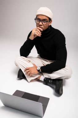 Şık bir genç adam yerde oturuyor, şık giyinmiş ve düşüncelere dalmış..