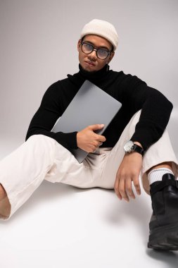 Şık giyinmiş yakışıklı genç bir adam dizüstü bilgisayarıyla rahatça oturur, kendine güveni ve yeteneği vardır..