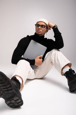 Şık bir genç adam dizüstü bilgisayarla yerde oturuyor, kendine güveni tam.