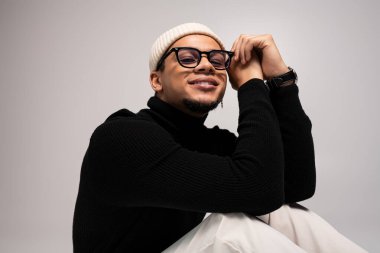 Modayı takip eden genç bir adam şık bir şekilde poz veriyor. Parlak bir gülümseme, tarz ve kendine güveni yansıtıyor..