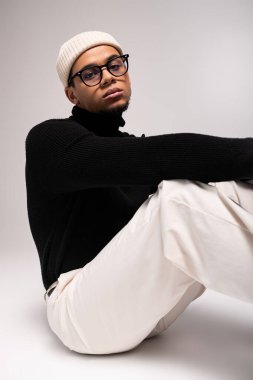 Şık giyinmiş genç bir adam düşünceli, göz alıcı bir moda ve bireysellik sergiliyor..