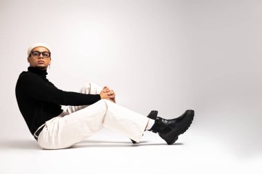 Genç adam şık kıyafetler içinde rahatlıyor, zarafeti şık bir ortamda sıradan bir havayla birleştiriyor..