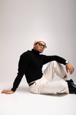 Tarz sahibi genç bir adam, sade bir yüzeyde otururken yaratıcı bir şekilde modayla poz verir..